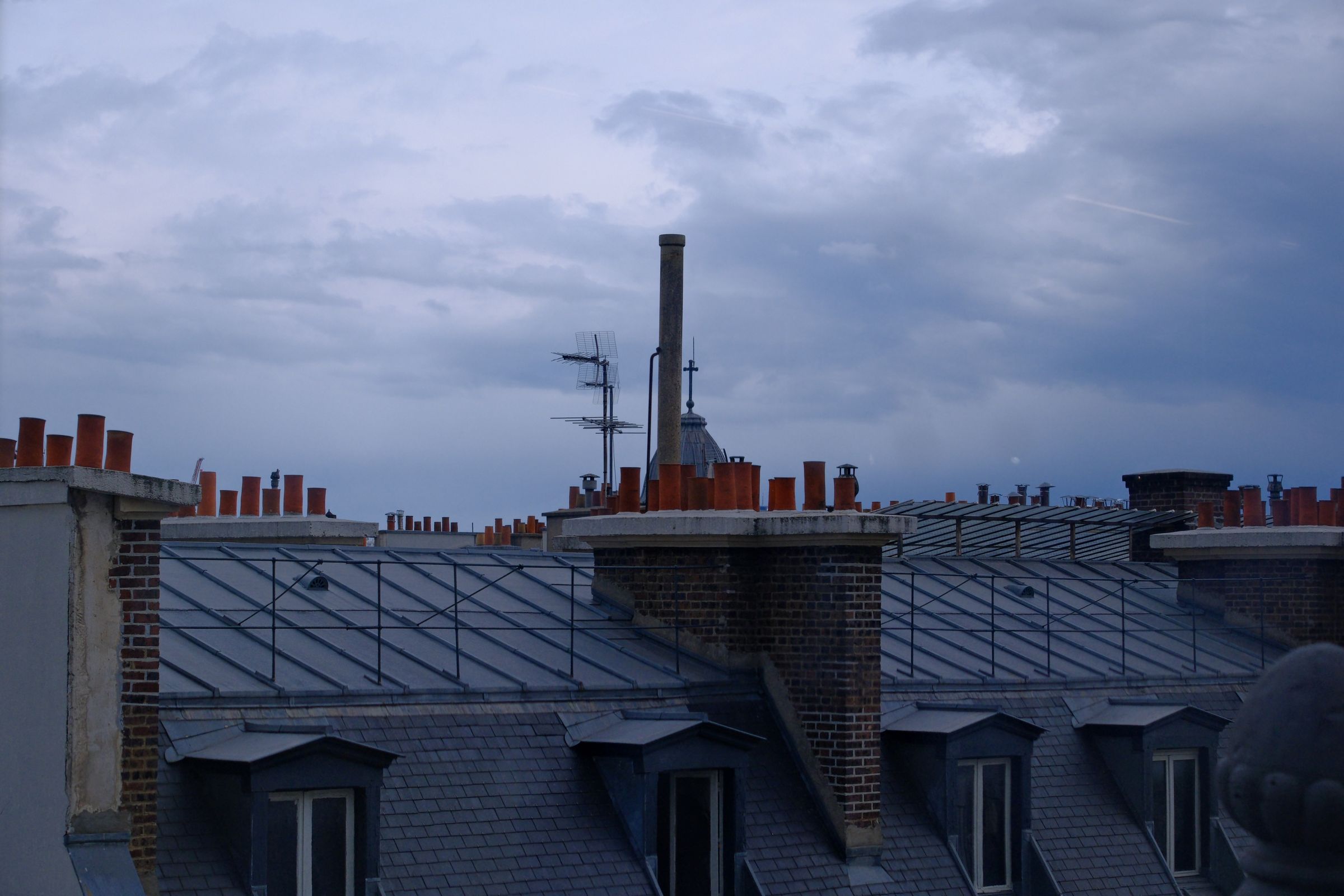 Toits parisiens en zinc, souches de cheminée en terre cuite et lucarnes d’ardoise au crépuscule